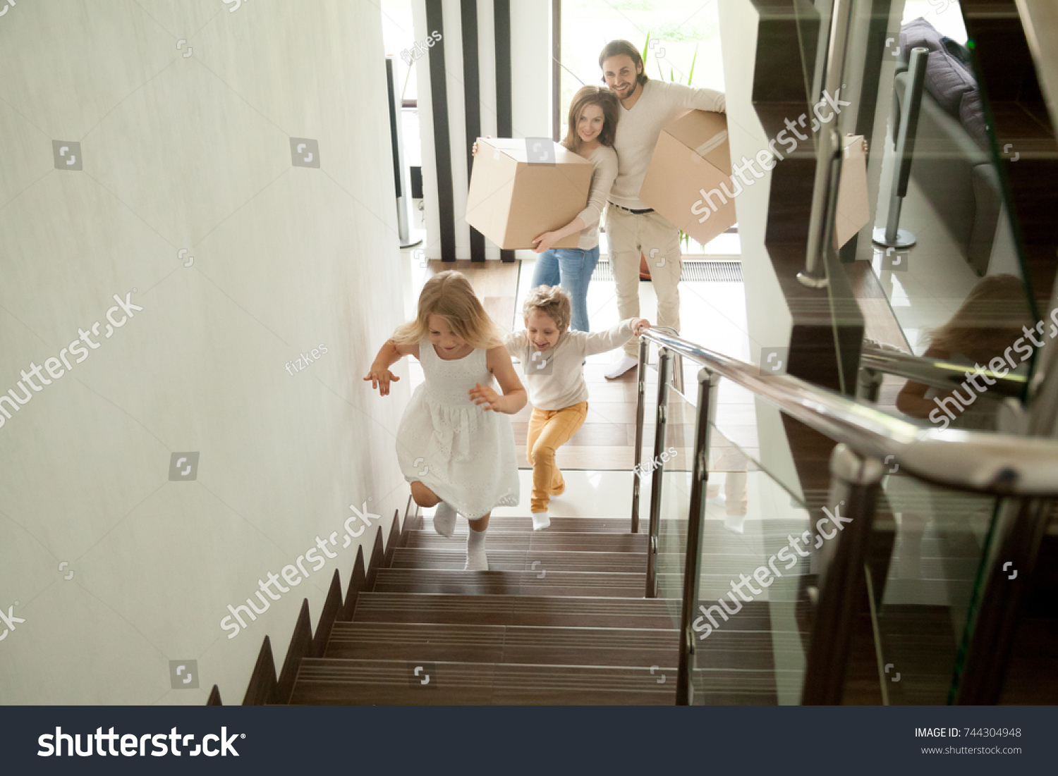 Happy children going upstairs inside two story big house, excited kids having fun stepping walking up stairs running to their rooms while parents holding boxes, family moving in relocating new home  #744304948