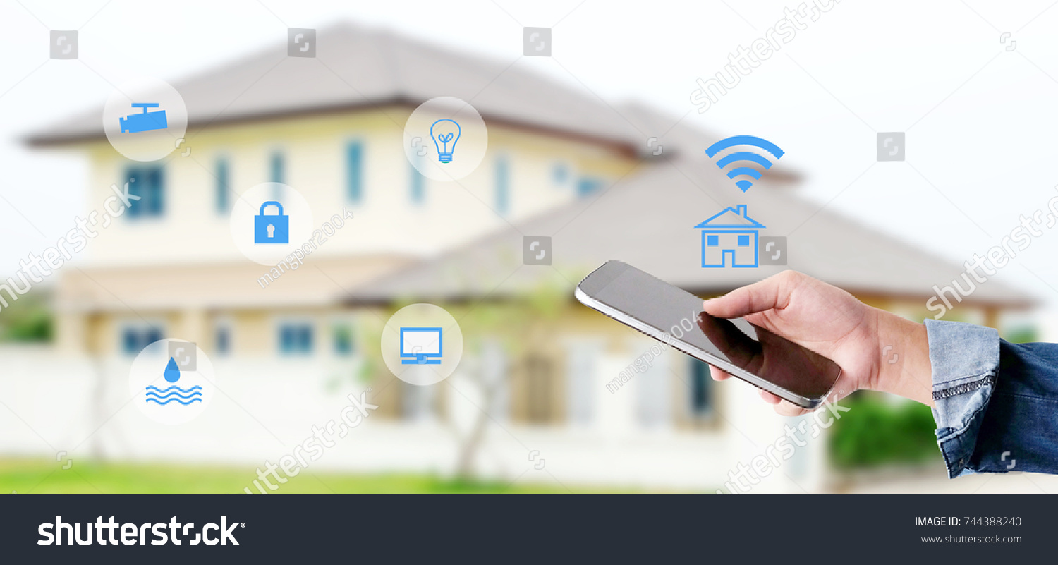 Hand using smart phone as smart home control application over blurred house background, banner, smart home concept #744388240