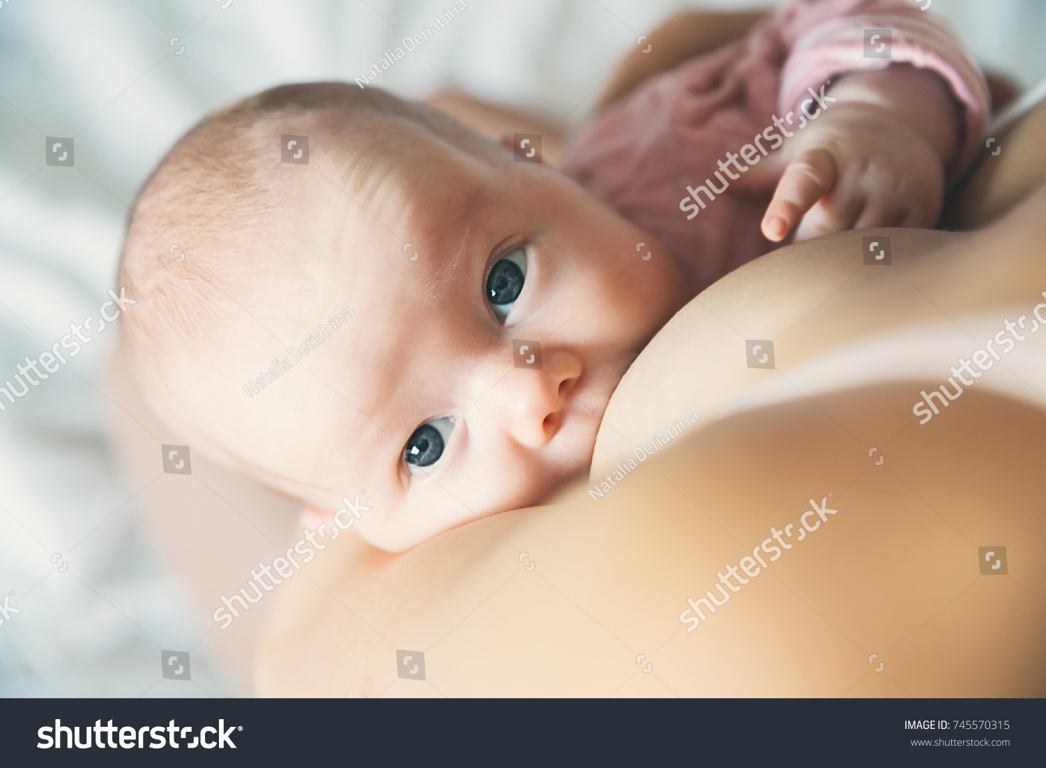 Baby eating mother's milk. Mother breastfeeding baby. Beautiful mom breast feeding her newborn child. Young woman nursing and feeding baby. Concept of lactation infant. #745570315