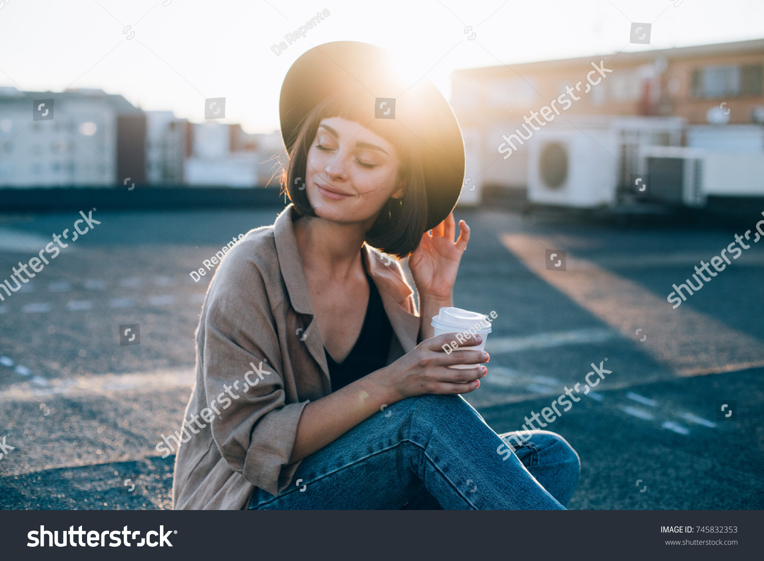 Portrait of beautiful young woman, in cute and adorable outfit, linen coat and fedora stylish fashion hat, drinks coffee from to go take away cup in amazing sunset light flares  #745832353