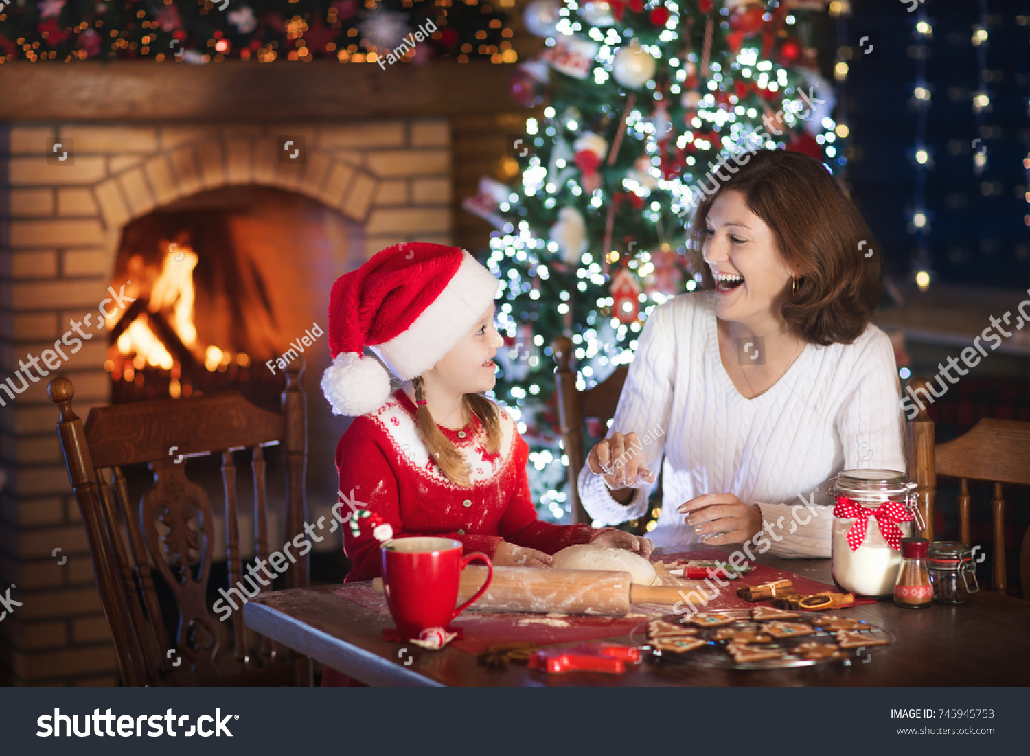 Mother and daughter baking Christmas cookies at fire place and decorated tree. Mom and child bake Xmas sweets. Family with kids celebrating Christmas at home. Little girl cooking in the kitchen. #745945753