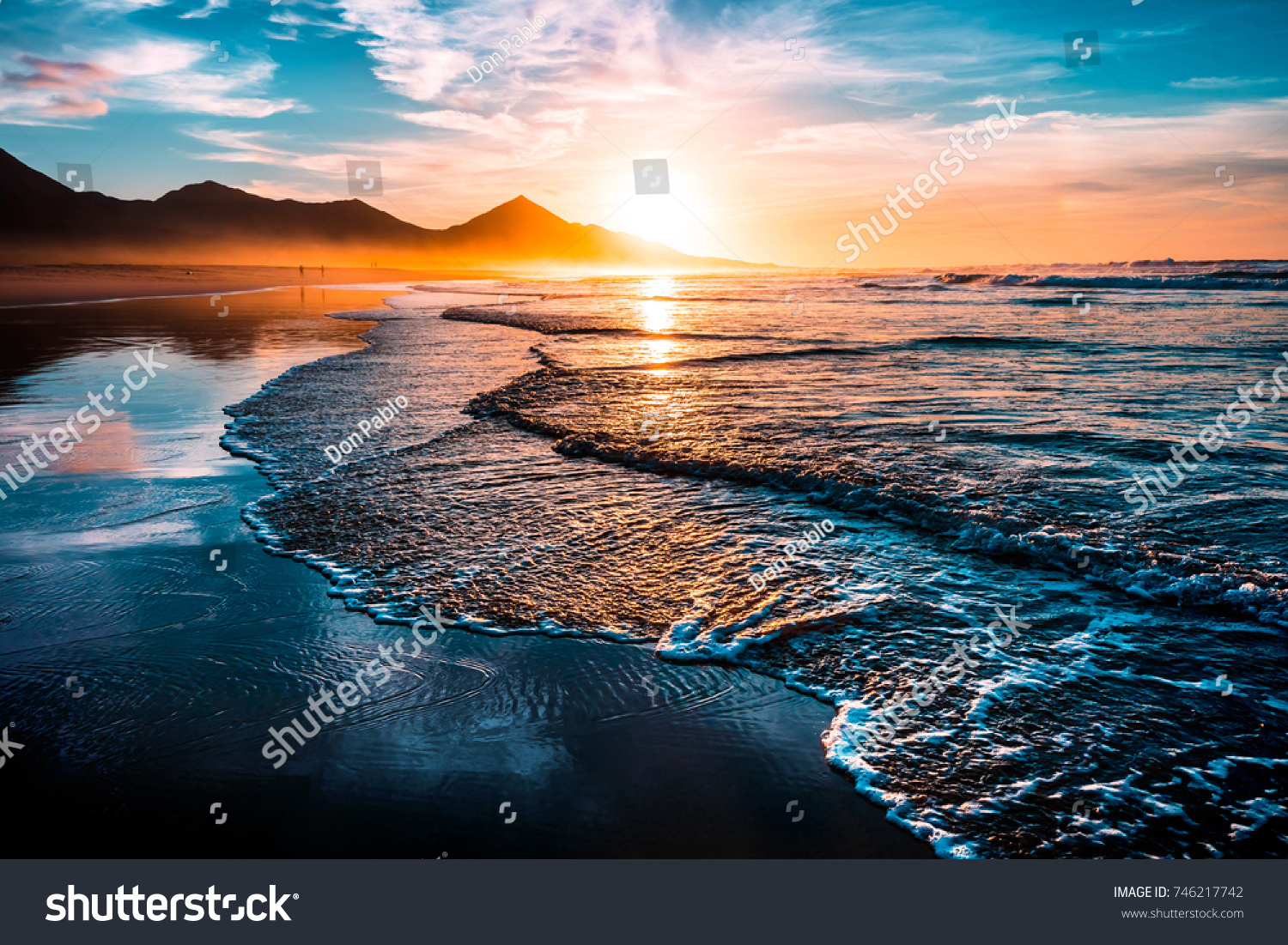 Amazing beach sunset with endless horizon and lonely figures in the distance, and incredible foamy waves. Volcanic hills in the background. #746217742