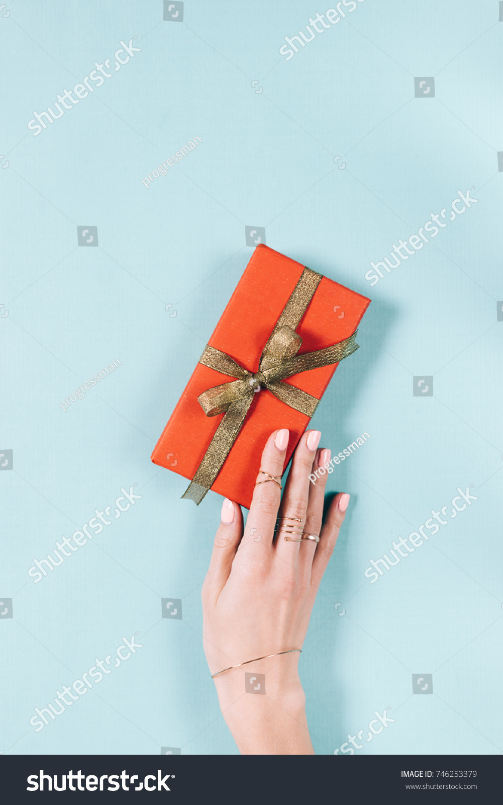Female hand and red gift box with golden ribbon on blue background top view #746253379
