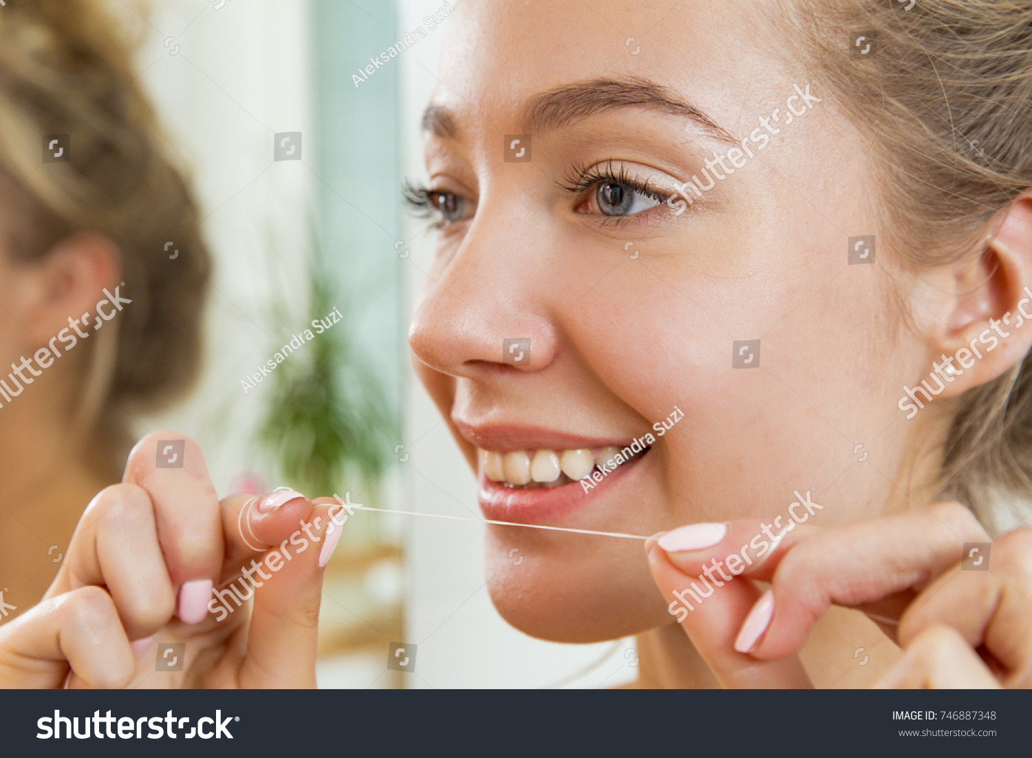 Young beautiful woman cleaning her teeth with floss in bathroom. Standing in towel, looking in the mirror, laughing and having fun. Daily routine. Beautiful smile with white teeth. #746887348