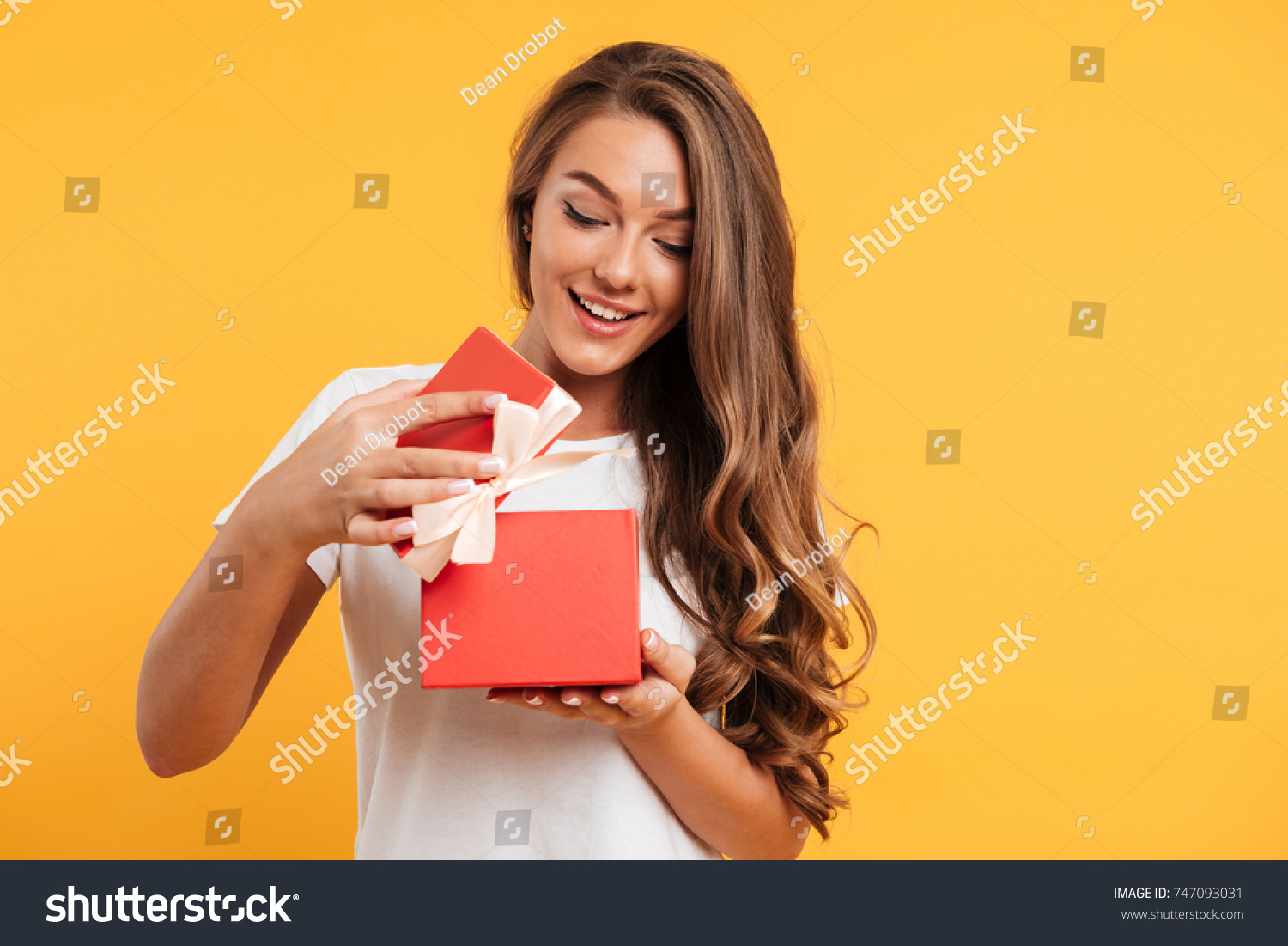 Portrait of a happy smiling girl opening a gift box isolated over yellow background #747093031