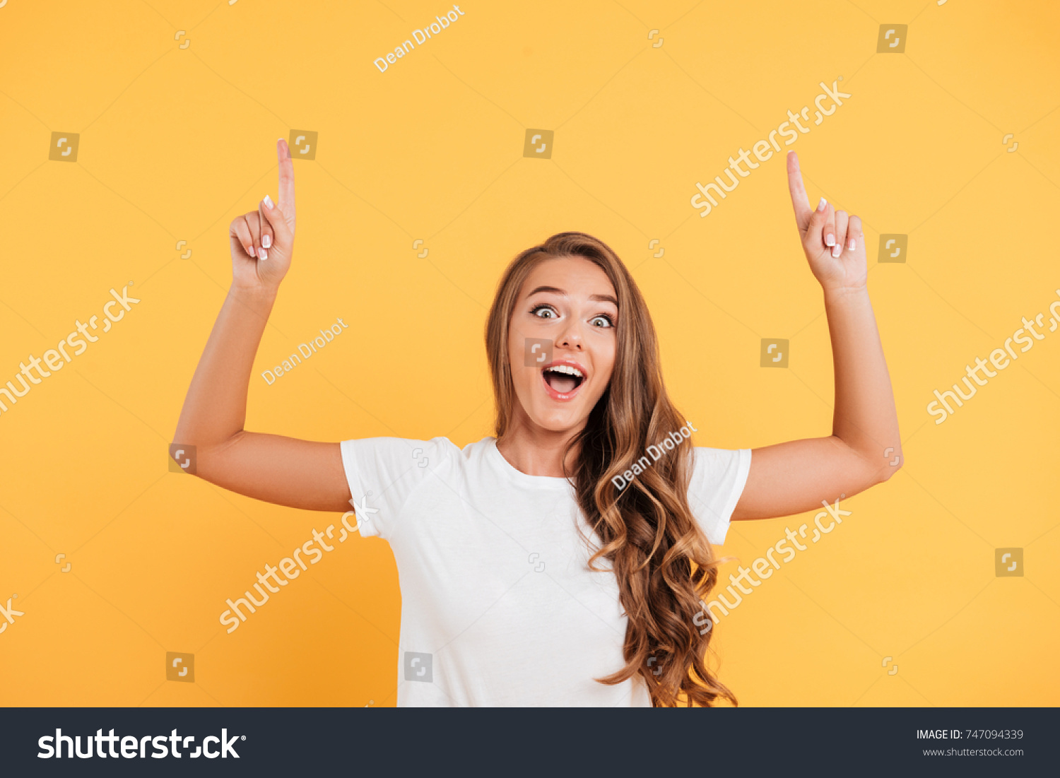 Photo of excited surprised beautiful young woman standing and posing isolated over yellow wall background. Looking camera and pointing to copyspace. #747094339