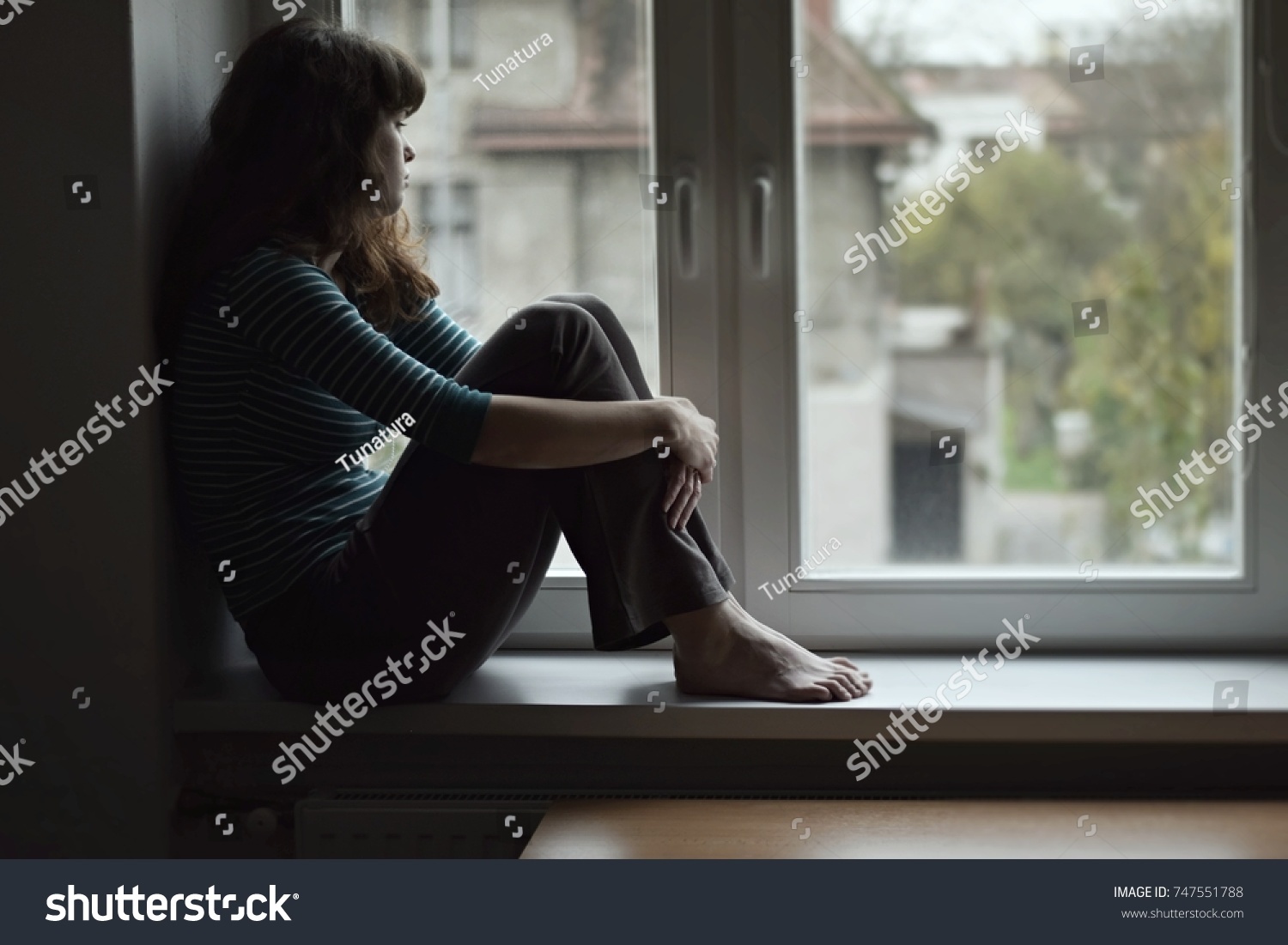 Sad young woman sitting on the window at home isolated, watching out. Coronavirus quarantine concept. #747551788