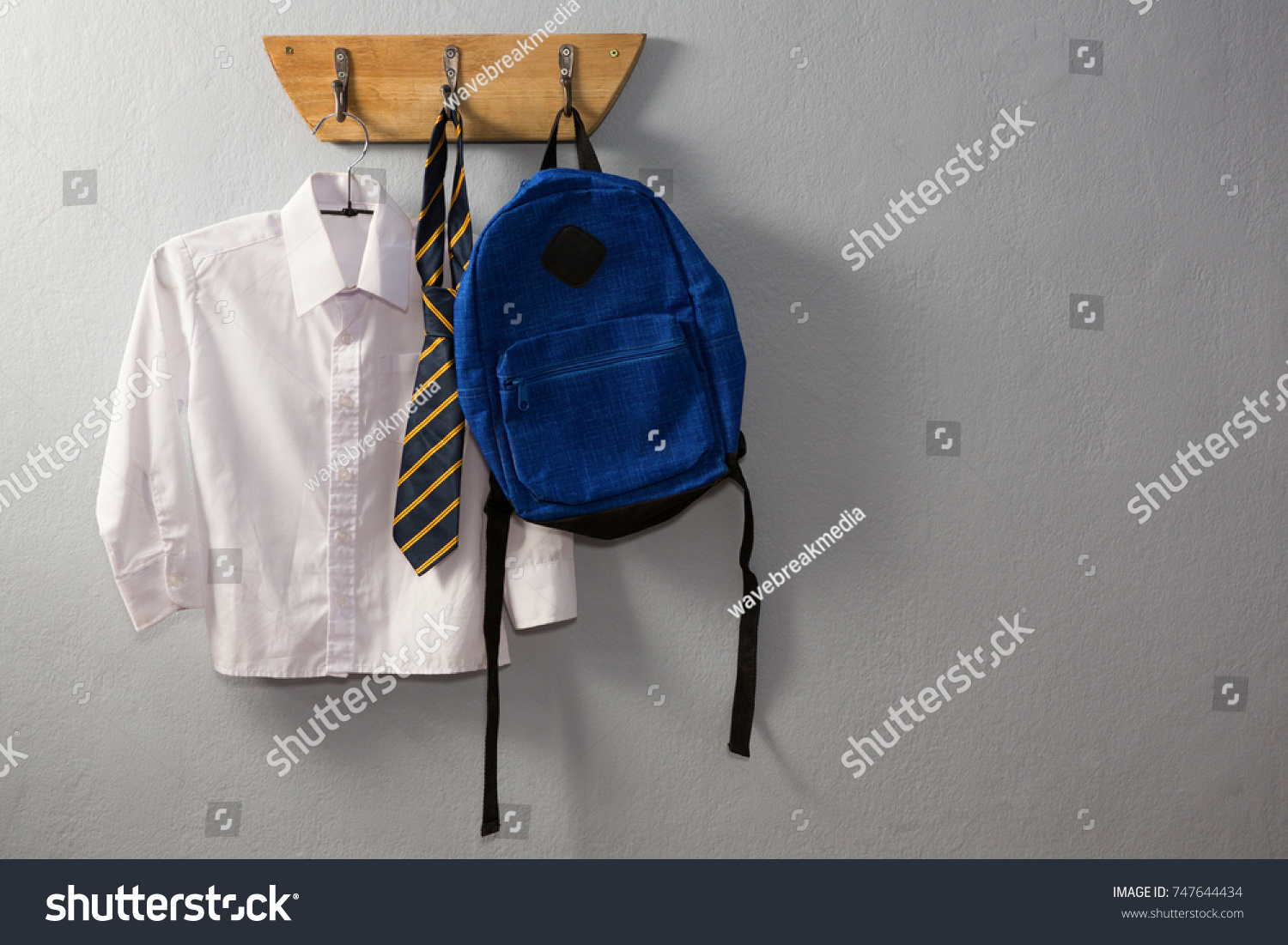 School uniform and schoolbag hanging on hook against wall #747644434