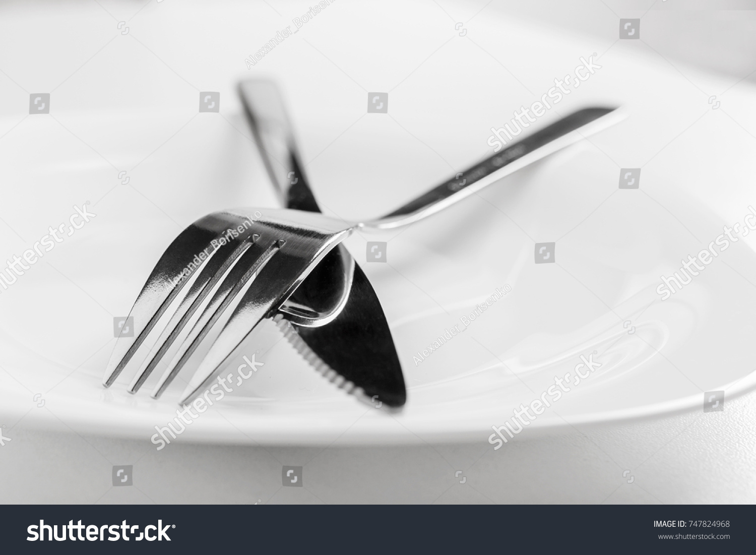 An empty plate, fork and knife lie crosswise on a white background. The dish did not like table etiquette #747824968