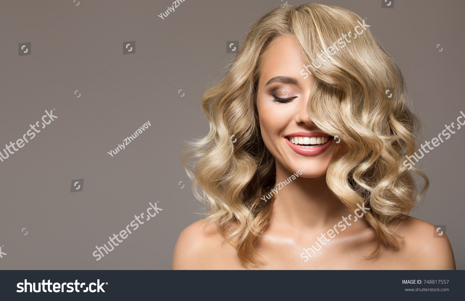 Blonde woman with curly beautiful hair smiling on gray background.  #748817557