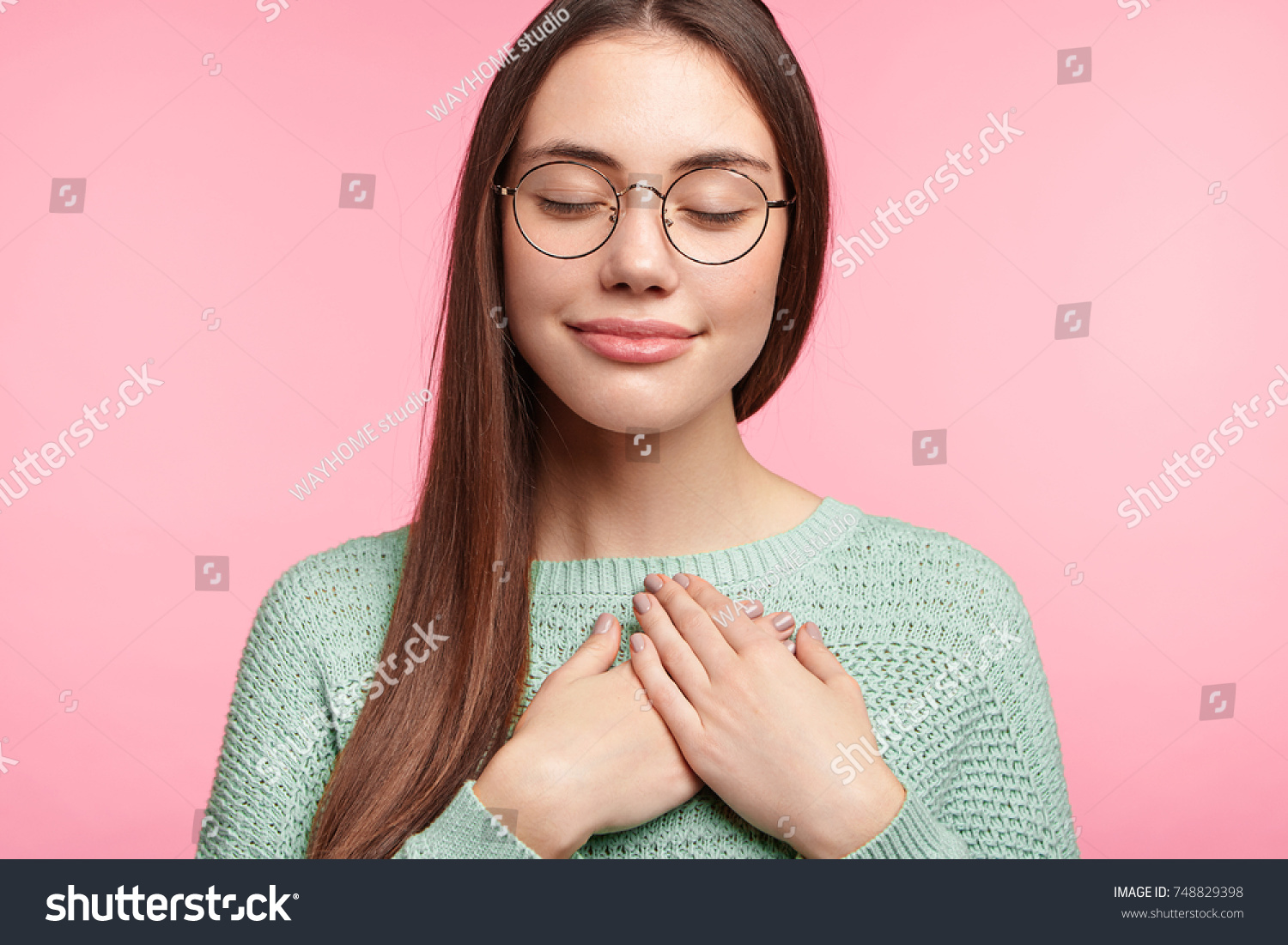Faithful woman closes eyes and keeps hands on chest near heart, shows her kindness or favour, expresses sincere emotions, being kind hearted and honest. Body language and real feelings concept #748829398