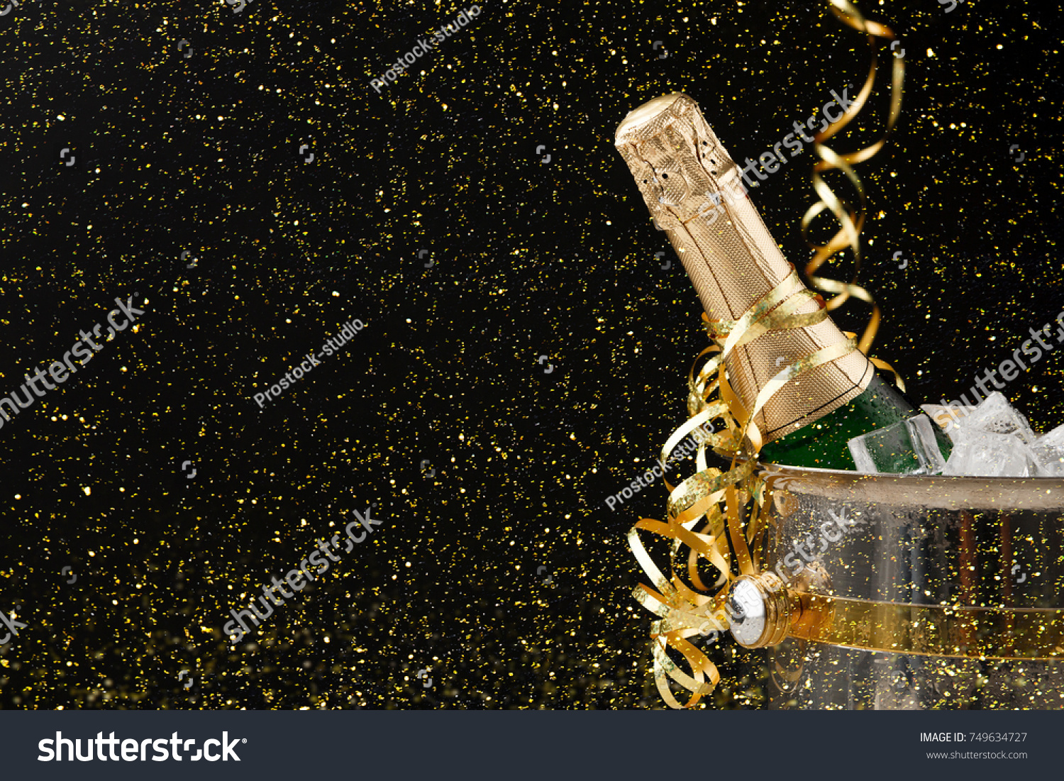 Celebrating new year, birthday, xmas party. Bottle of champagne in a bucket and colorful tinsel on black backgroud with golden glitters, copy space. Mockup for postcard #749634727