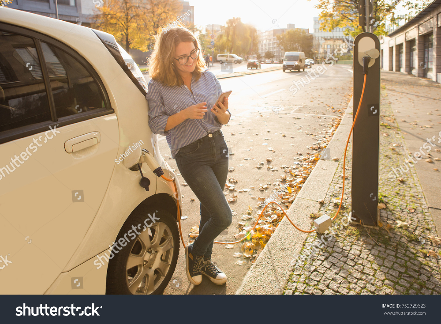 Woman with phone near an rental electric car. Vehicle charged at the charging station. #752729623