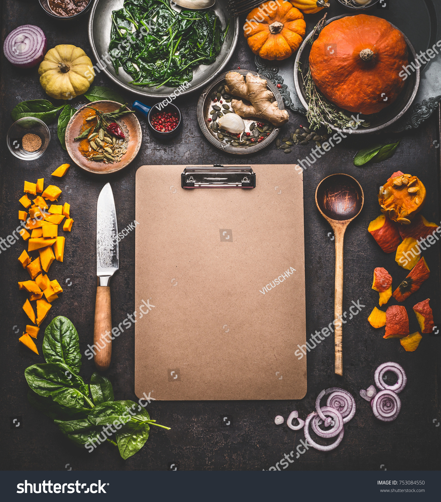Food background for tasty winter and autumn dishes with pumpkin. Various cooking ingredients with spoon and knife around blank cardboard clipboard for menu or recipes , top view, frame, mock up #753084550