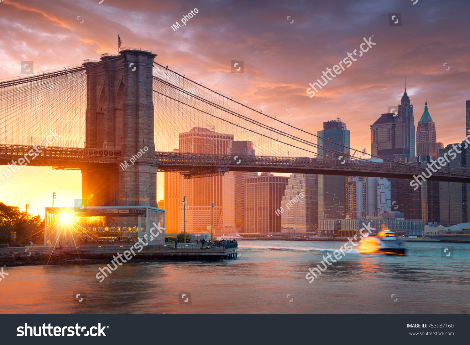 Famous Brooklyn Bridge in New York City with financial district - downtown Manhattan in background. Sightseeing boat on the East River and beautiful sunset over Jane's Carousel. #753987160