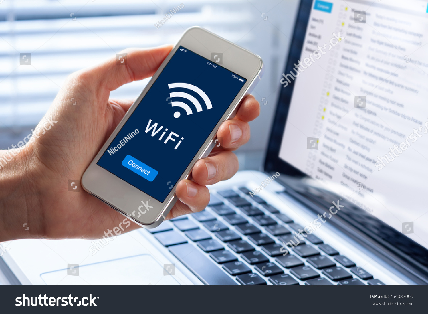 WiFi symbol on smartphone screen with button to connect to wireless internet, close-up of hand holding mobile phone, computer in background #754087000