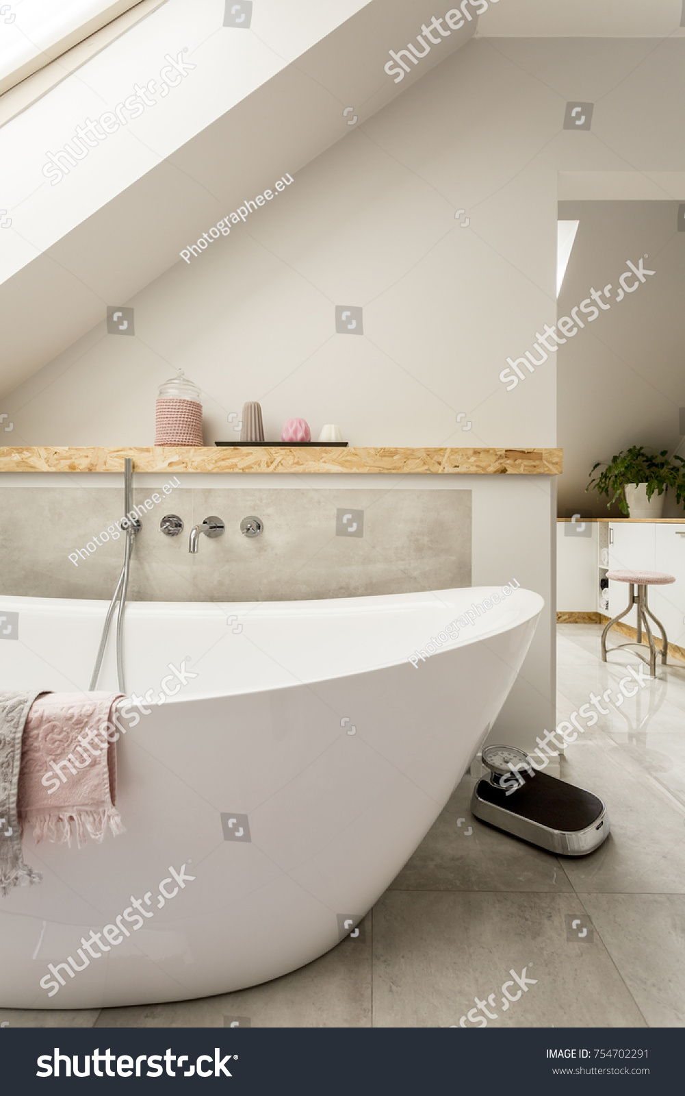 White bathtub next to a shelf with candles in monochromatic bathroom in the attic #754702291