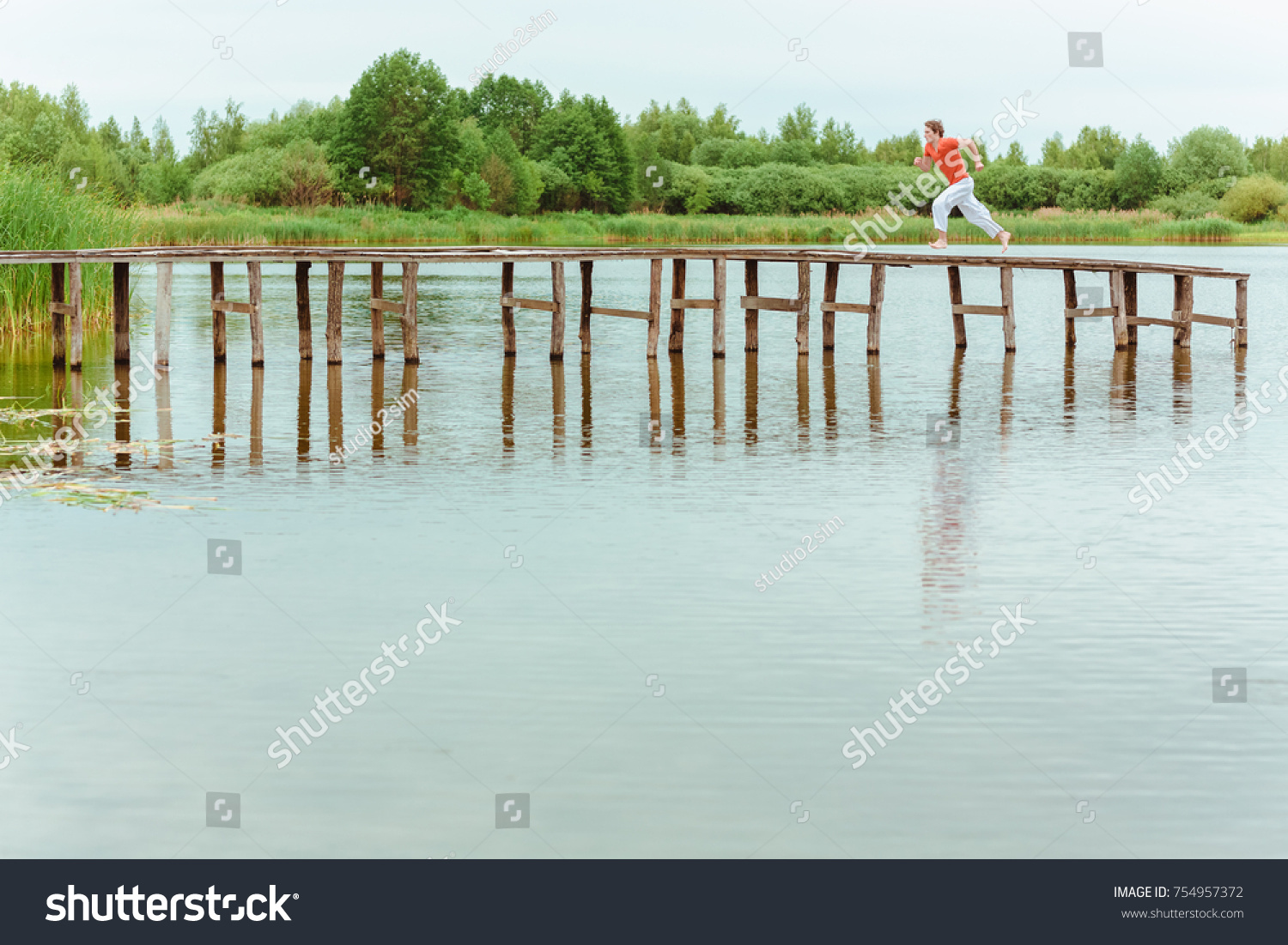 Man running on wooden pier at lake #754957372