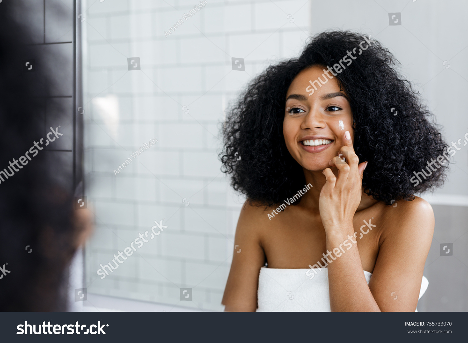 Happy young woman applying face cream with finger in bathroom #755733070