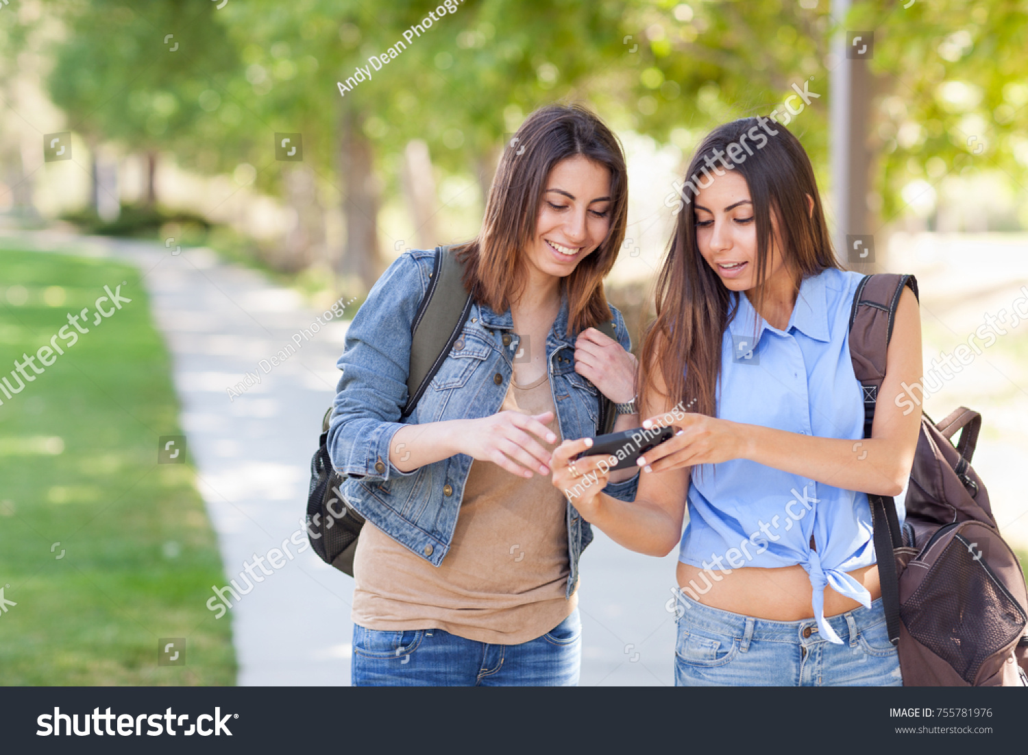 Two Beautiful Young Ethnic Twin Sisters With Backpacks Using A Smartphone Outside. #755781976