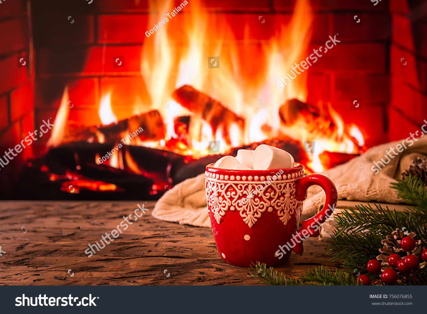 Mug of hot chocolate or coffee with marshmallows in a red mug on vintage wood table in front of Fireplace as a background. Christmas or winter warming drink. #756076855