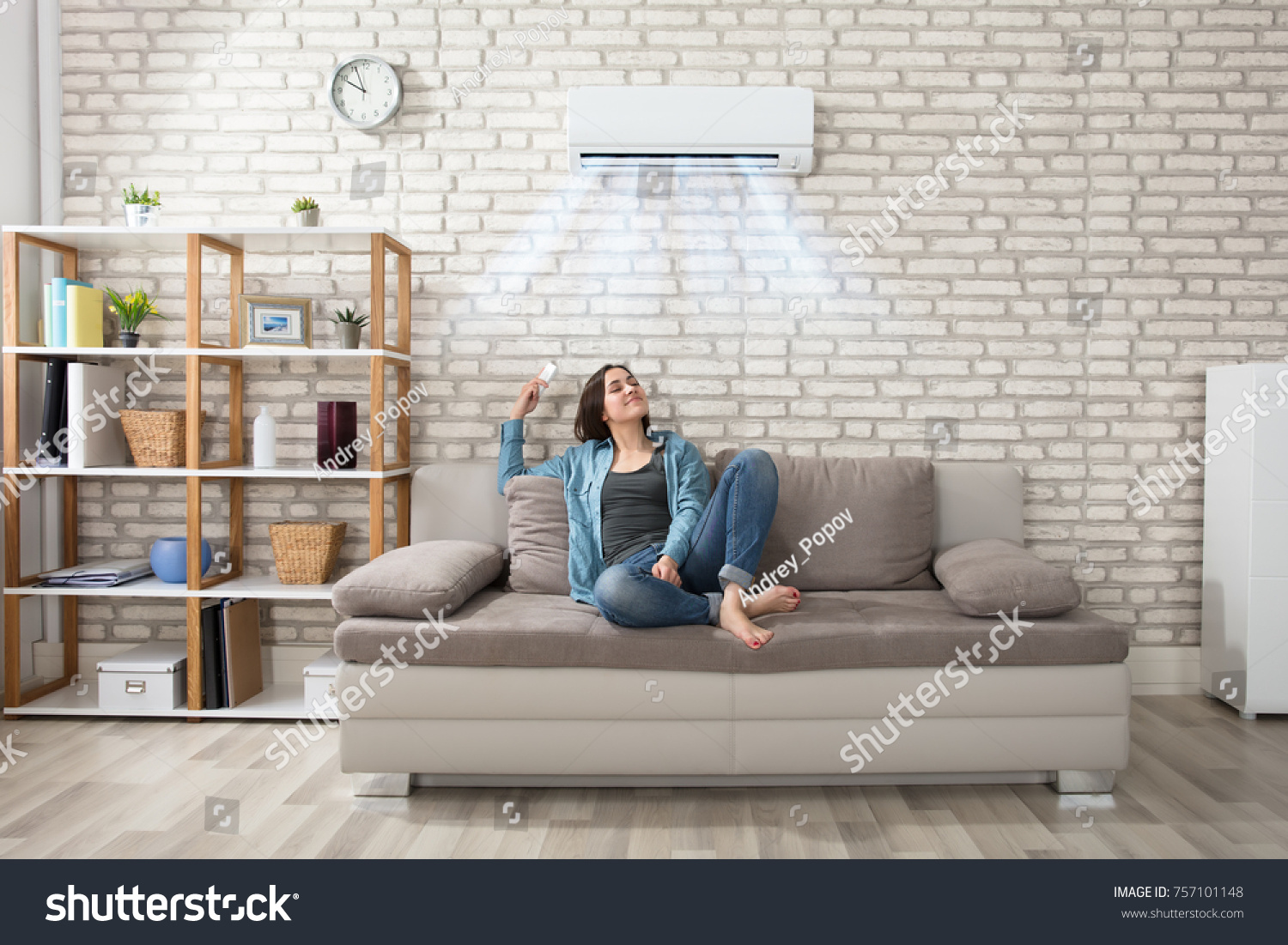 Happy Young Woman Holding Remote Control Relaxing Under The Air Conditioner #757101148