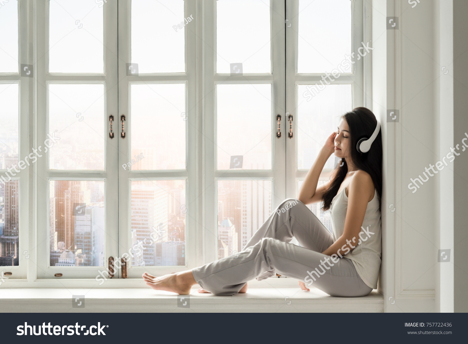 A cute Asian girl is listening a classic song in front of white window in a holiday of weekend . #757722436