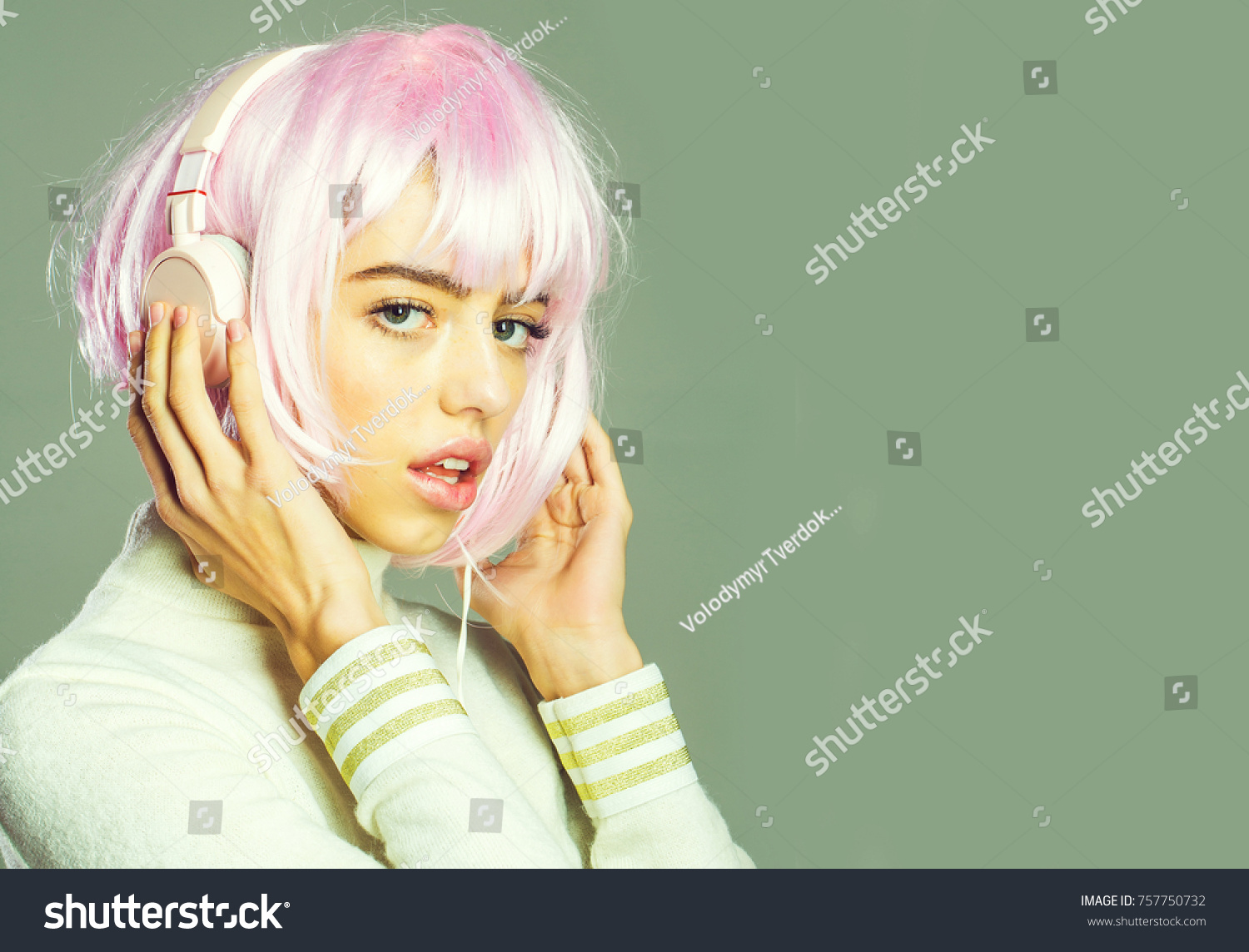 young pretty woman or cute sexy girl with pink glamour hair wig in fashionable shirt, poses on grey background with music headset, copy space #757750732