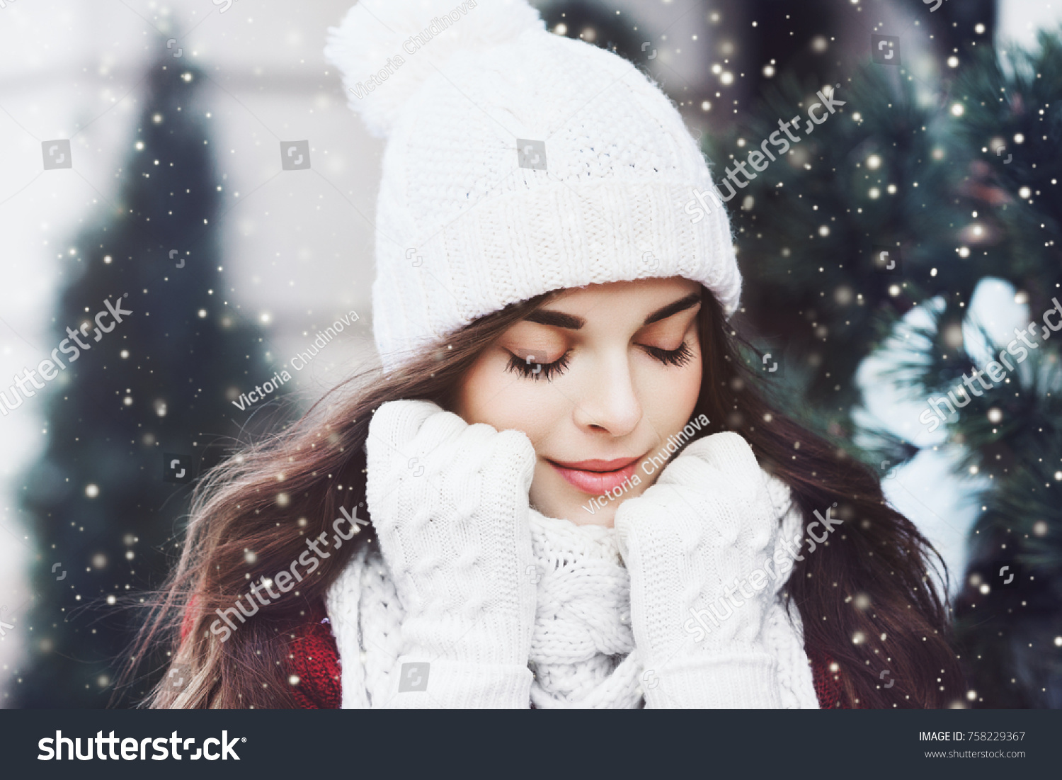 Outdoor close up portrait of young beautiful happy smiling girl wearing white knitted beanie hat, scarf and gloves. Model posing in street. Winter holidays concept. Toned #758229367