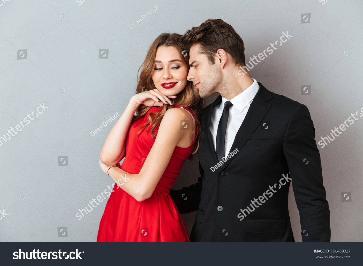 Portrait of a lovely attractive couple dressed in formal wear posing while standing and hugging over gray wall background #760489327