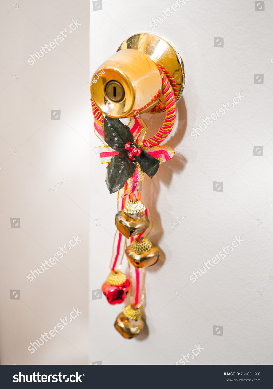 Close-up photograph of red and gold colored Christmas bells hanging on a polished brass colored door knob for festive holiday background image. #760651600