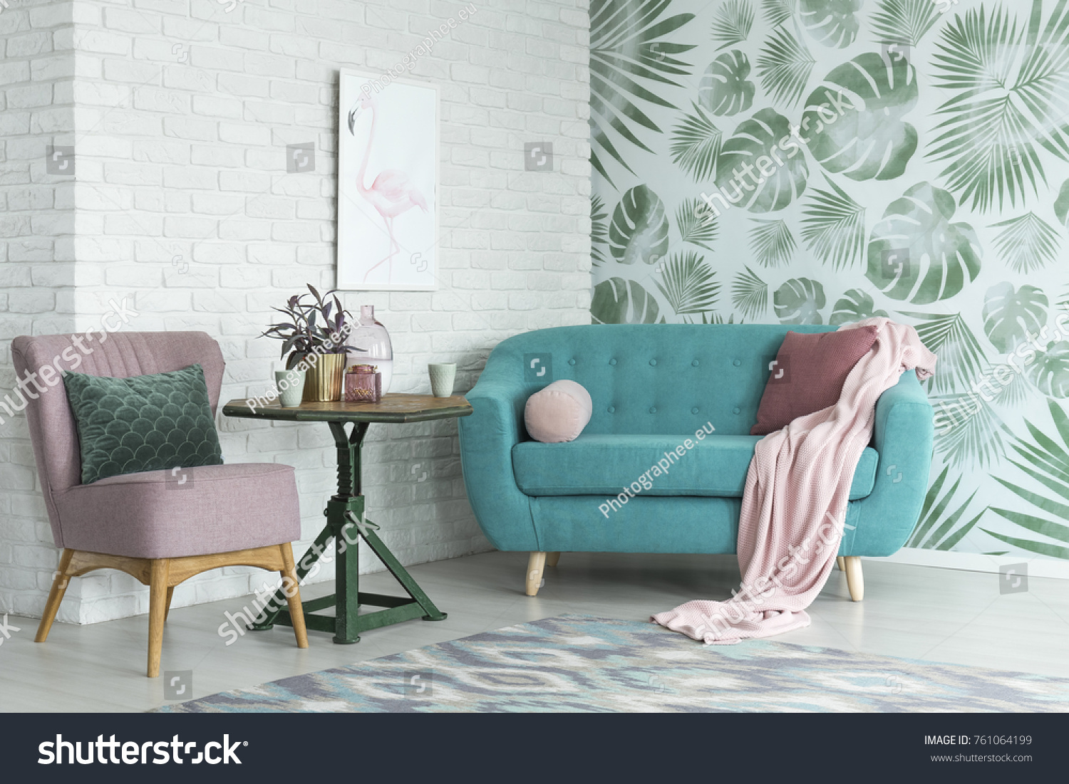 Green table with a plant between pink chair and blue sofa in floral living room with wallpaper and poster