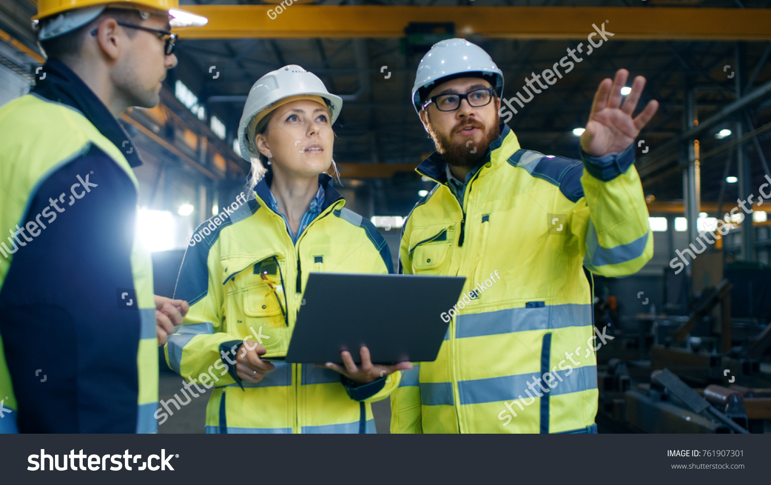 Male and Female Industrial Engineers Talk with Factory Worker while Using Laptop. They Work at the Heavy Industry Manufacturing Facility. #761907301