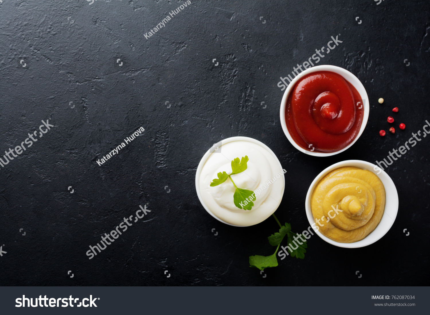 Set of three sauces - mayonnaise, mustard and ketchup in white ceramic bowls on  black stone or concrete background. Selective focus. Top view. #762087034
