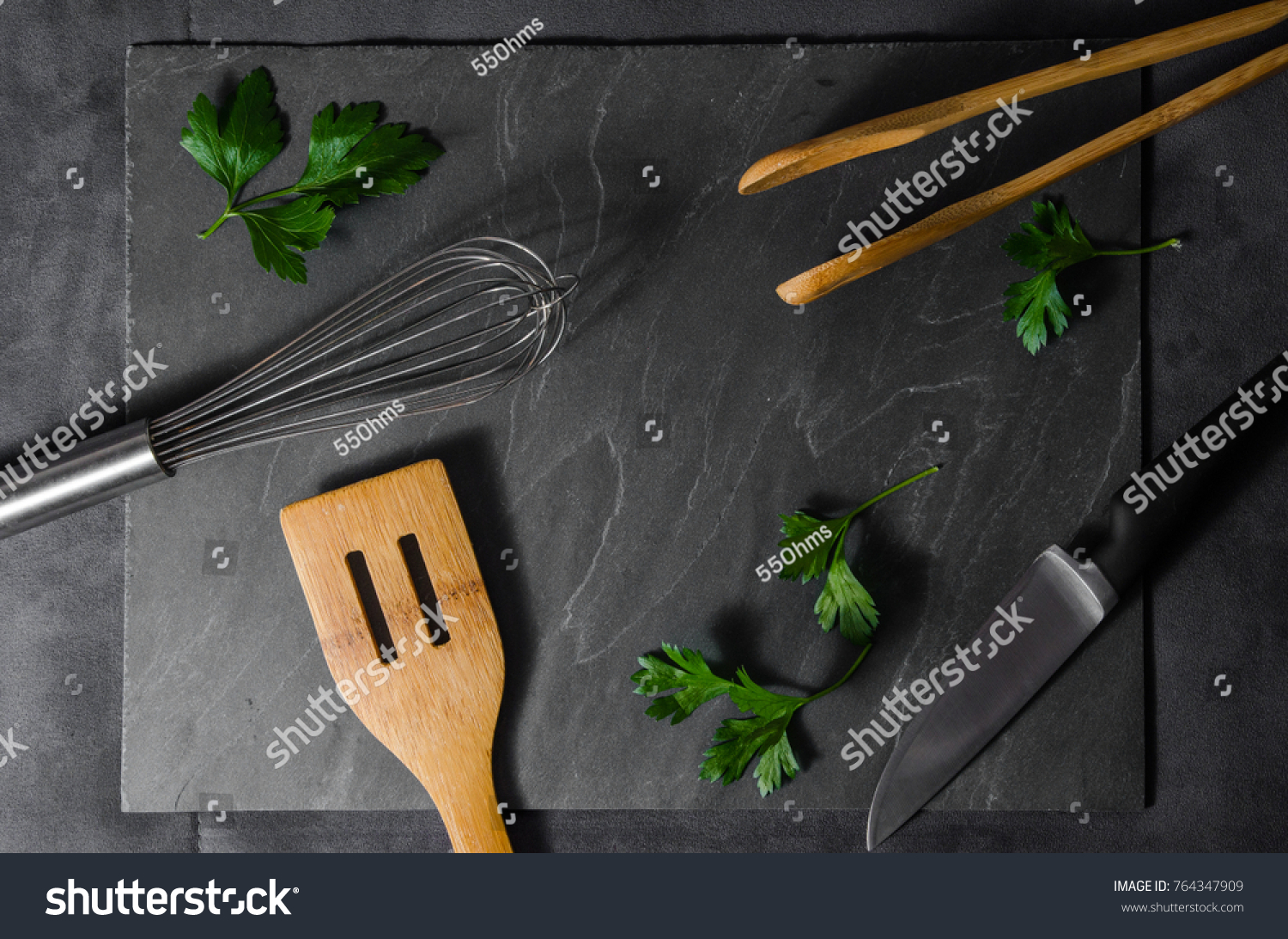Kitchen utensils layout with fresh green parsley leaves on dark grey stone background. Can be used for advertising, menus, brochures, food blogs. Studio lighting #764347909