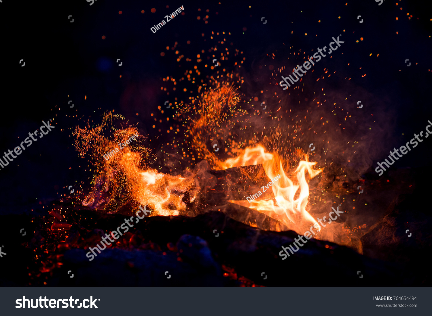 Burning woods with firesparks, flame and smoke. Strange weird odd elemental fiery figures on black background. Coal and ash. Abstract shapes at night. Bonfire outdoor on nature. Strenght of element #764654494
