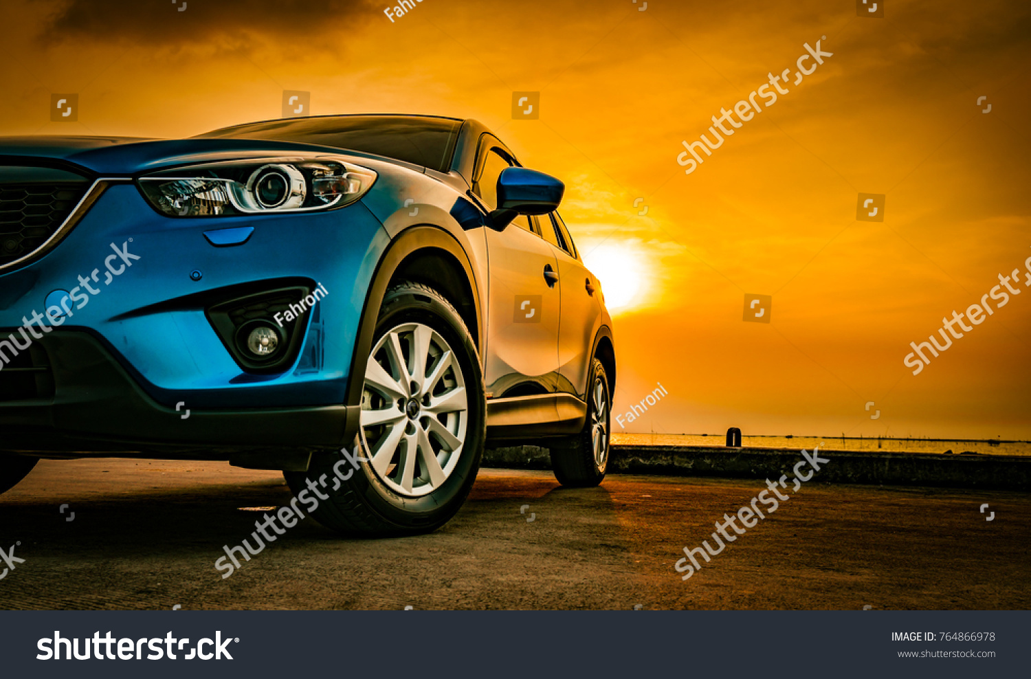 Blue compact SUV car with sport and modern design parked on concrete road by the sea at sunset. Environmentally friendly technology. Business success concept. #764866978