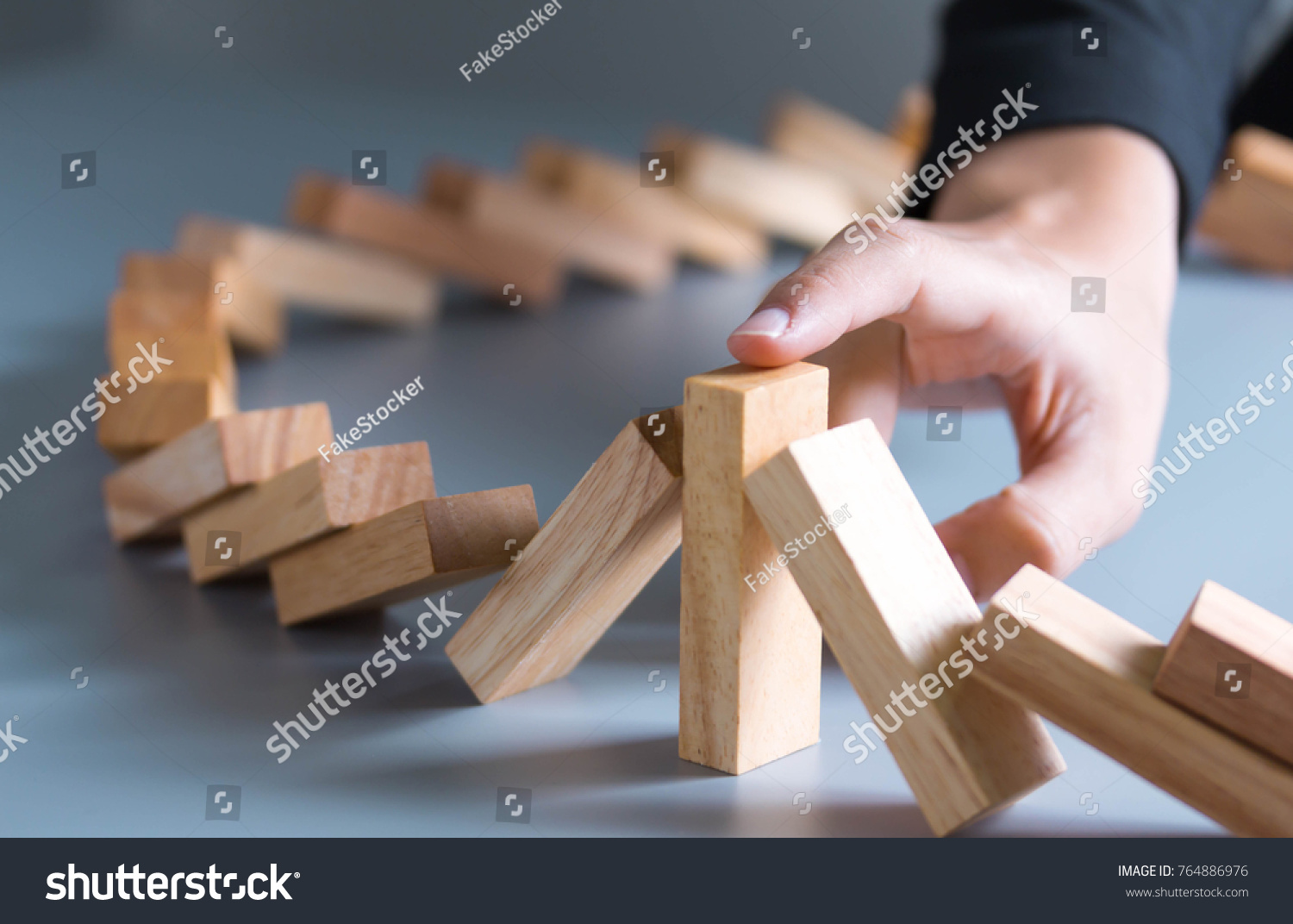 Close up of businessman hand Stopping Falling wooden Dominoes effect from continuous toppled or risk,
 strategy and successful intervention concept for business.
 #764886976