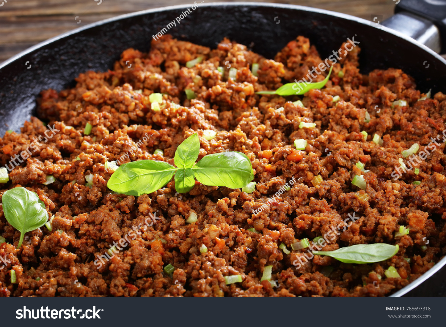 close-up of hot juicy ground beef stewed with tomato sauce, spices, basil, finely chopped vegetables and celery in frying pan, classic recipe, side view from above #765697318