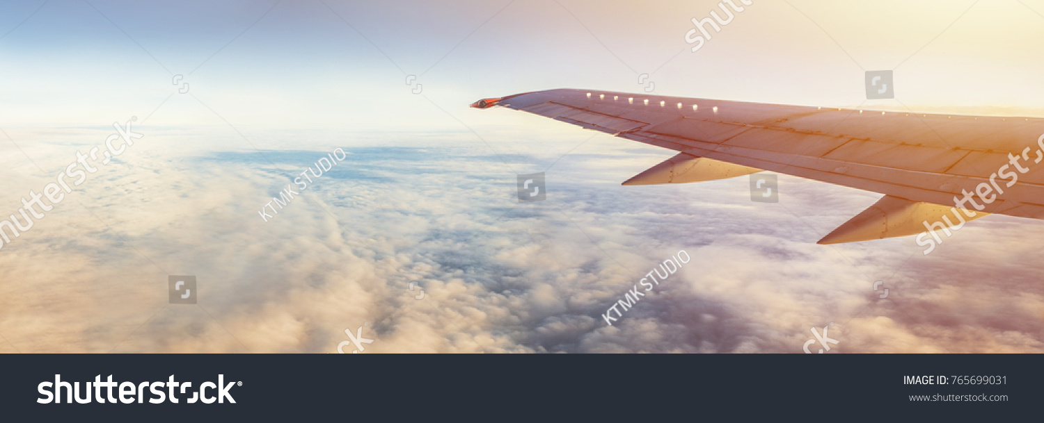 Flight wing panorama with copy space. Aircraft wing above the earth and clouds. Flight in sky. Travel by airlines for vacations. #765699031