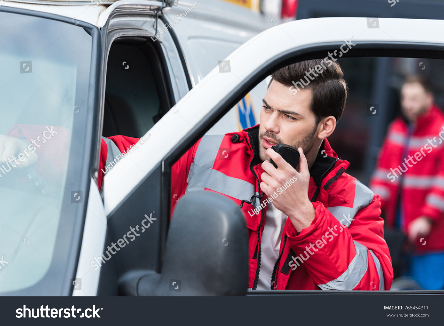 young handsome male paramedic standing near ambulance and talking by portable radio #766454311