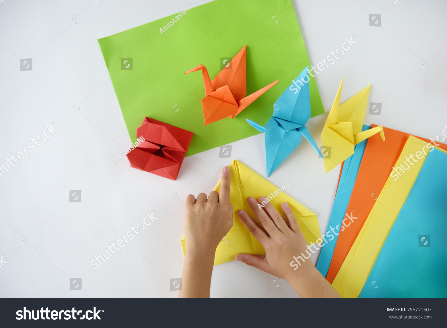 Children's hands do origami from colored paper on white background. lesson of origami #766770607