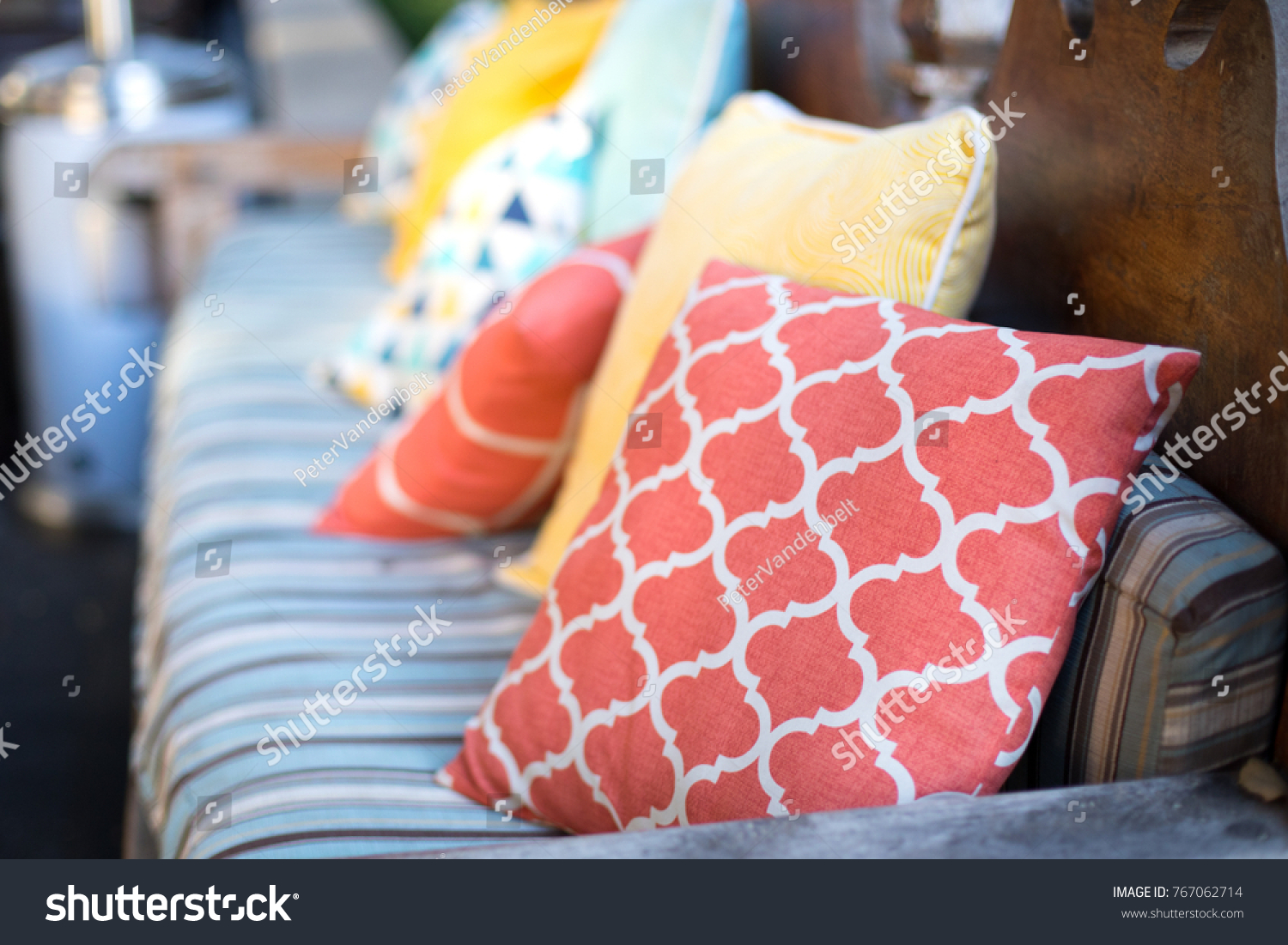 Close up on orange and yellow pattern throw pillows on an outdoor patio chair, with a blue striped cushioned bench  #767062714