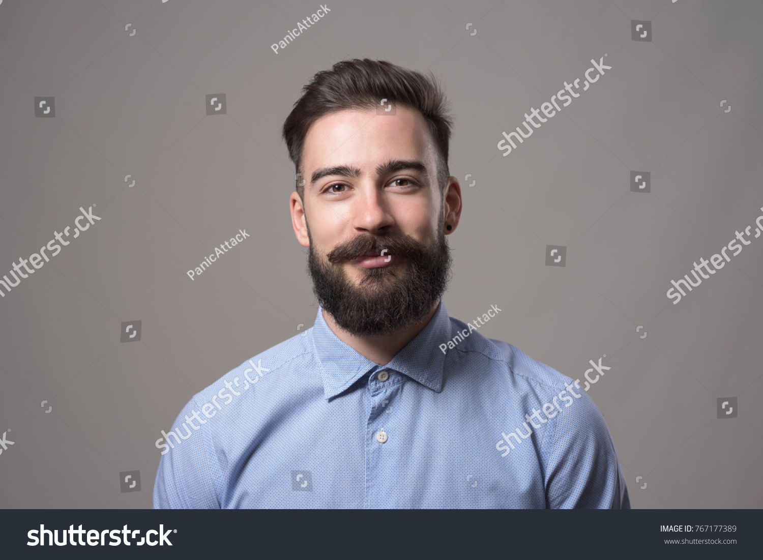 Horizontal  head and shoulder portrait of young bearded business man smiling at camera against gray studio background. #767177389