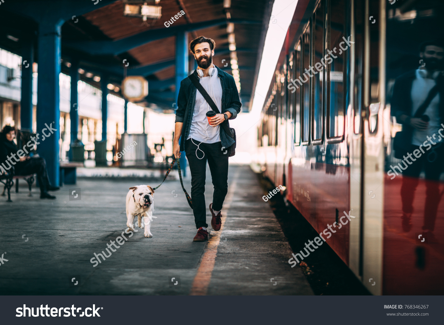 Young man going on vacation with train. Handsome guy walkiing with his bulldog at train station. #768346267