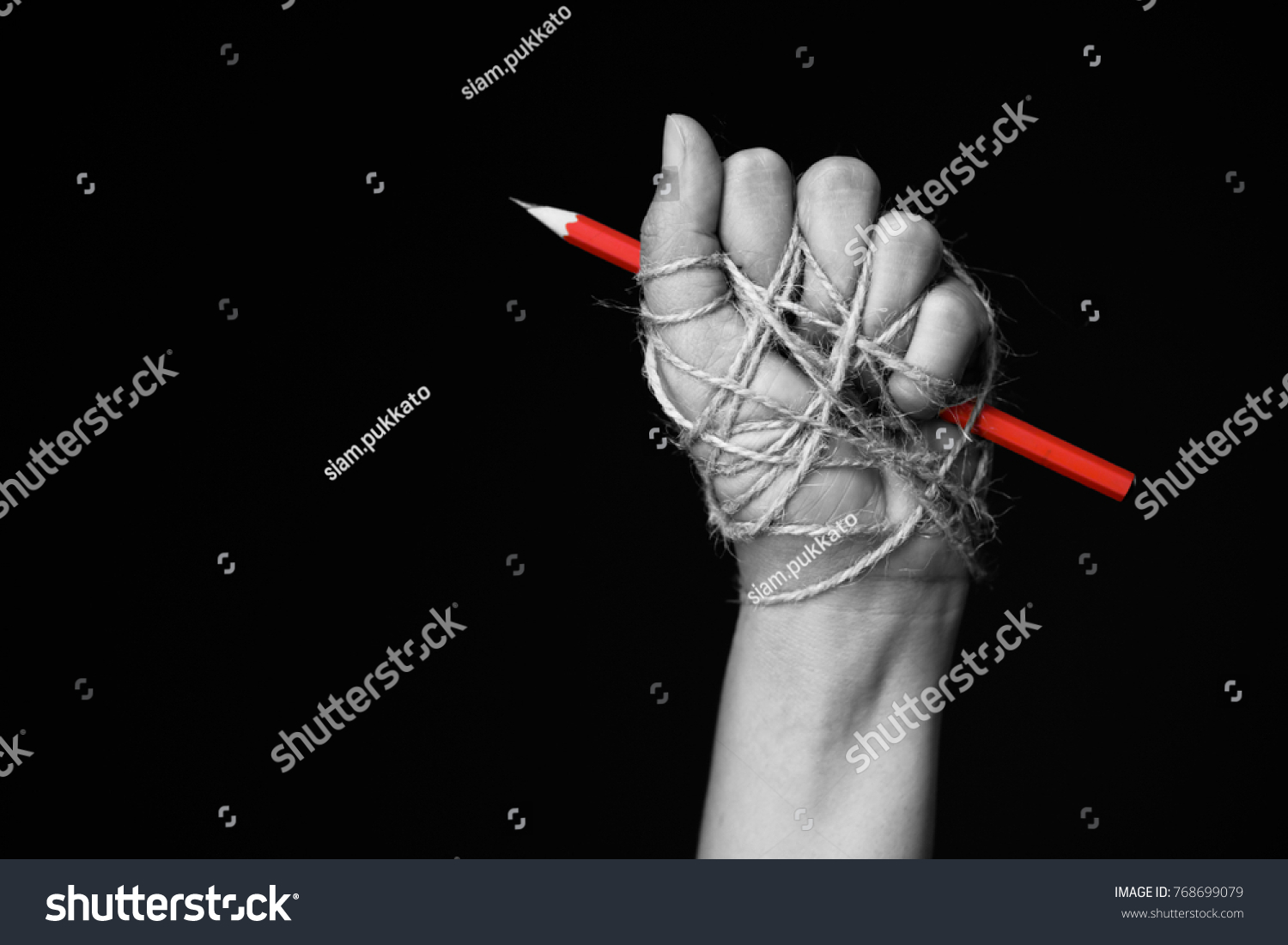 Hand with red pencil tied with rope, depicting the idea of freedom of the press or freedom of expression on dark background in low key. international human rights day concept. #768699079