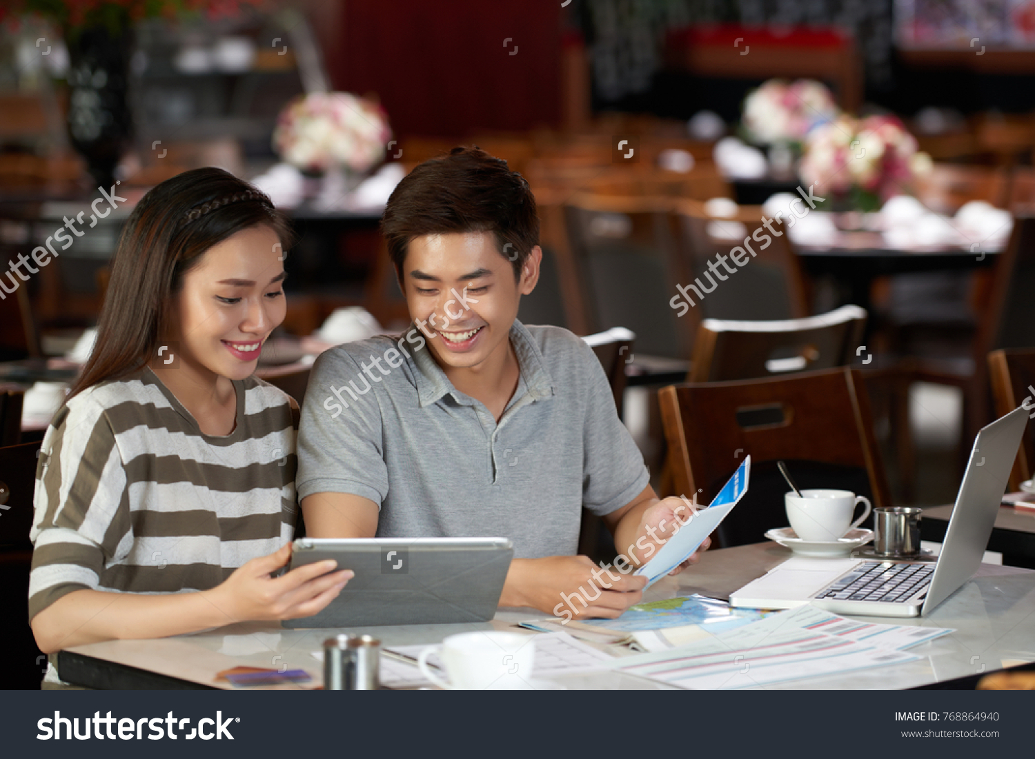 Planning trip to Europe: cheerful young couple sitting at spacious cafe while booking hotel and buying airline tickets online #768864940