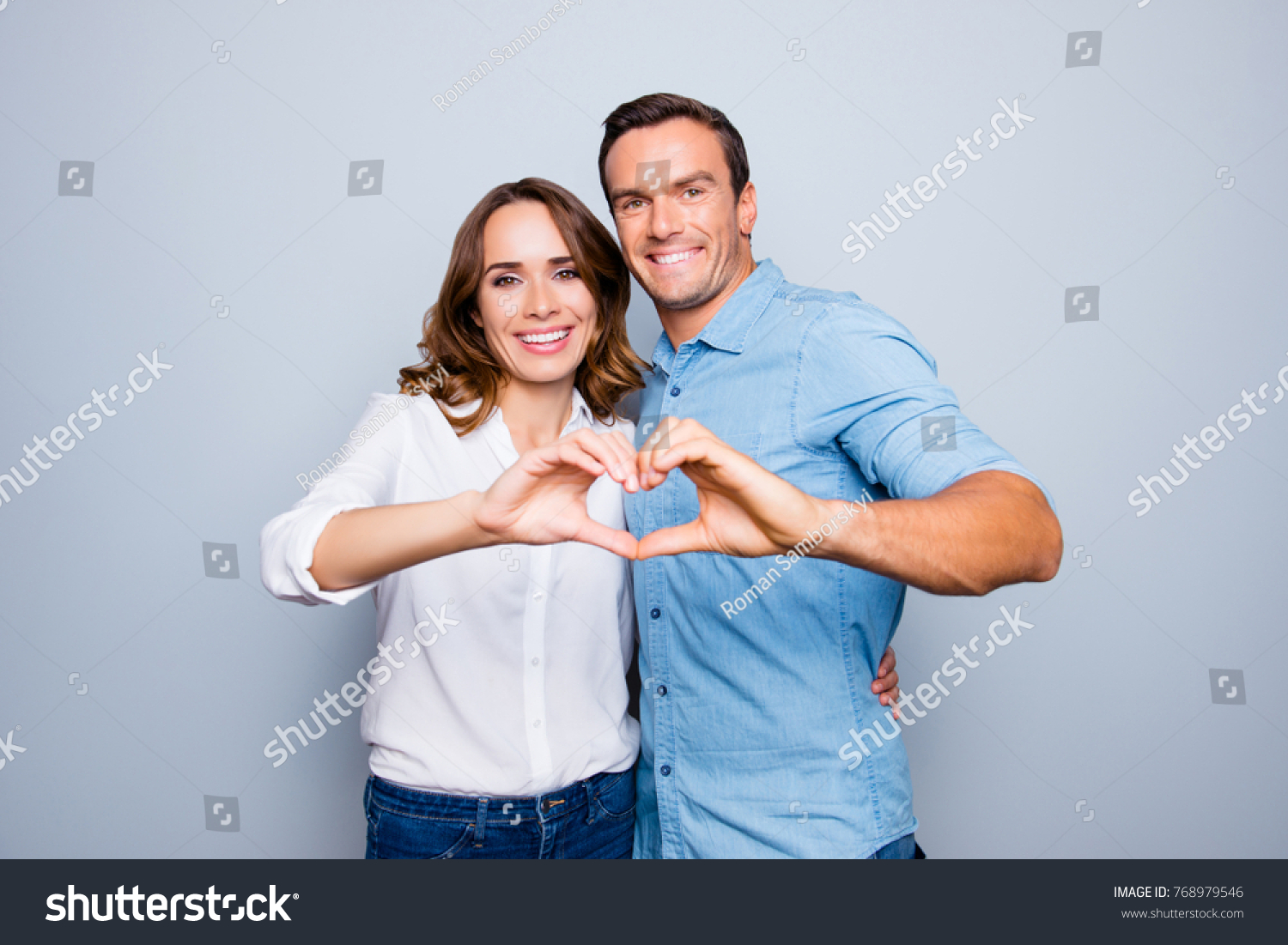 Love story of cheerful, attractive, mature, adult, lovely, cute, sweet couple in casual outfit, jeans, shirt making heart with fingers over grey background #768979546
