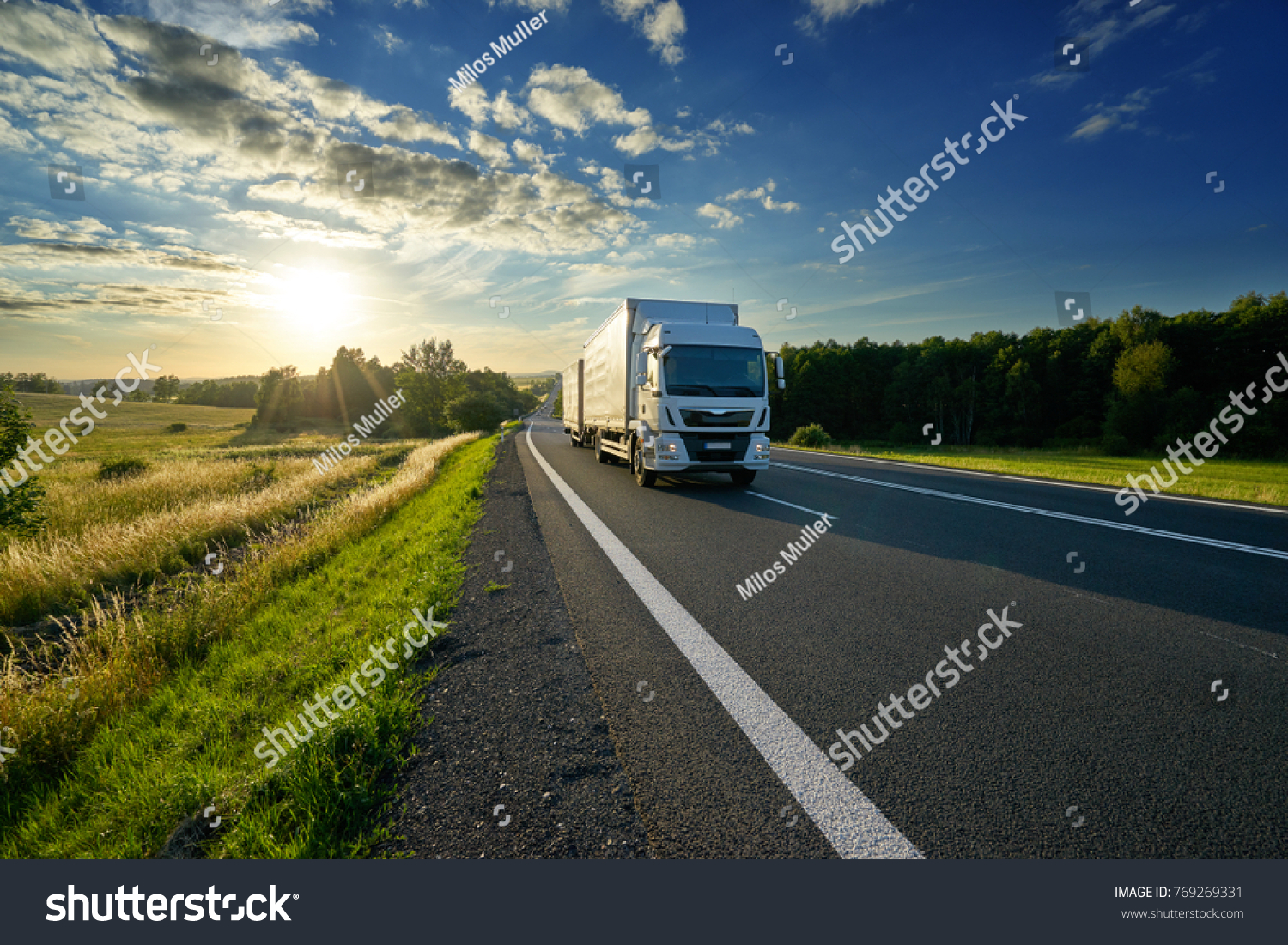 White delivery truck driving on the asphalt road in rural landscape at sunset #769269331