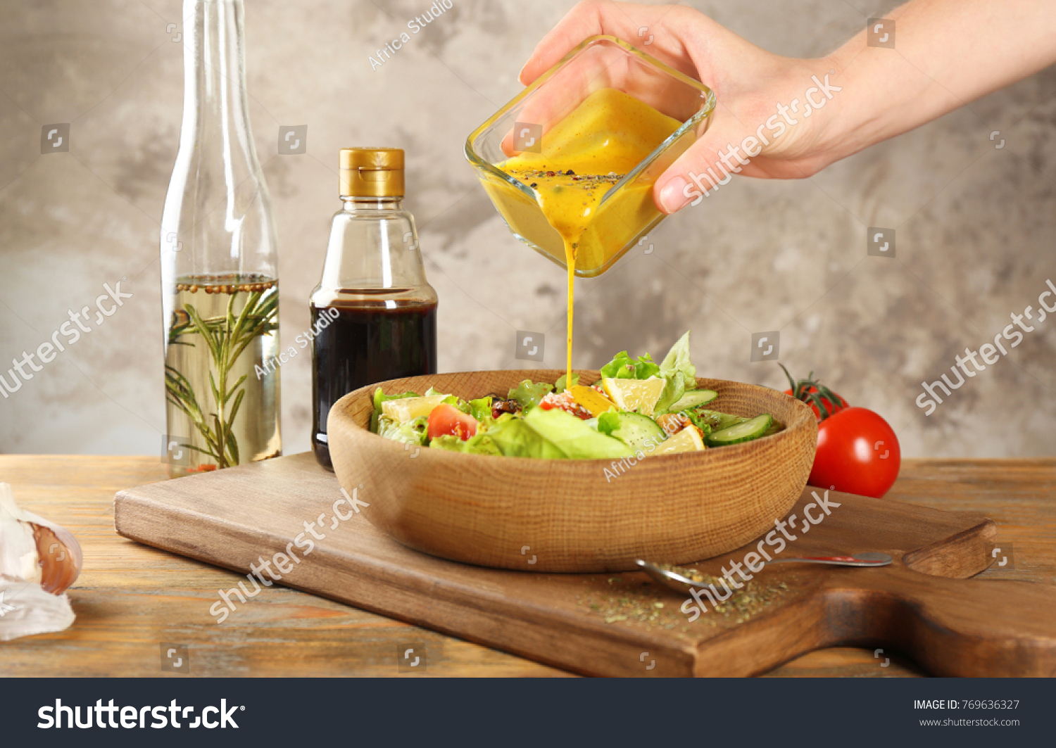 Woman pouring honey mustard dressing into bowl with fresh salad on table #769636327